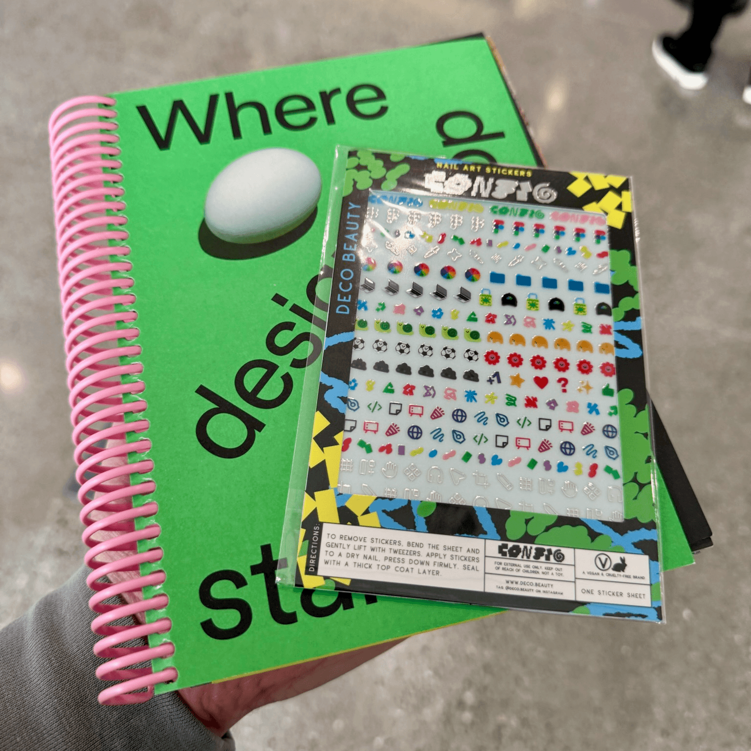 A green Config 2026 art book titled 'Where design starts' next to a sheet of Config-branded nail art stickers