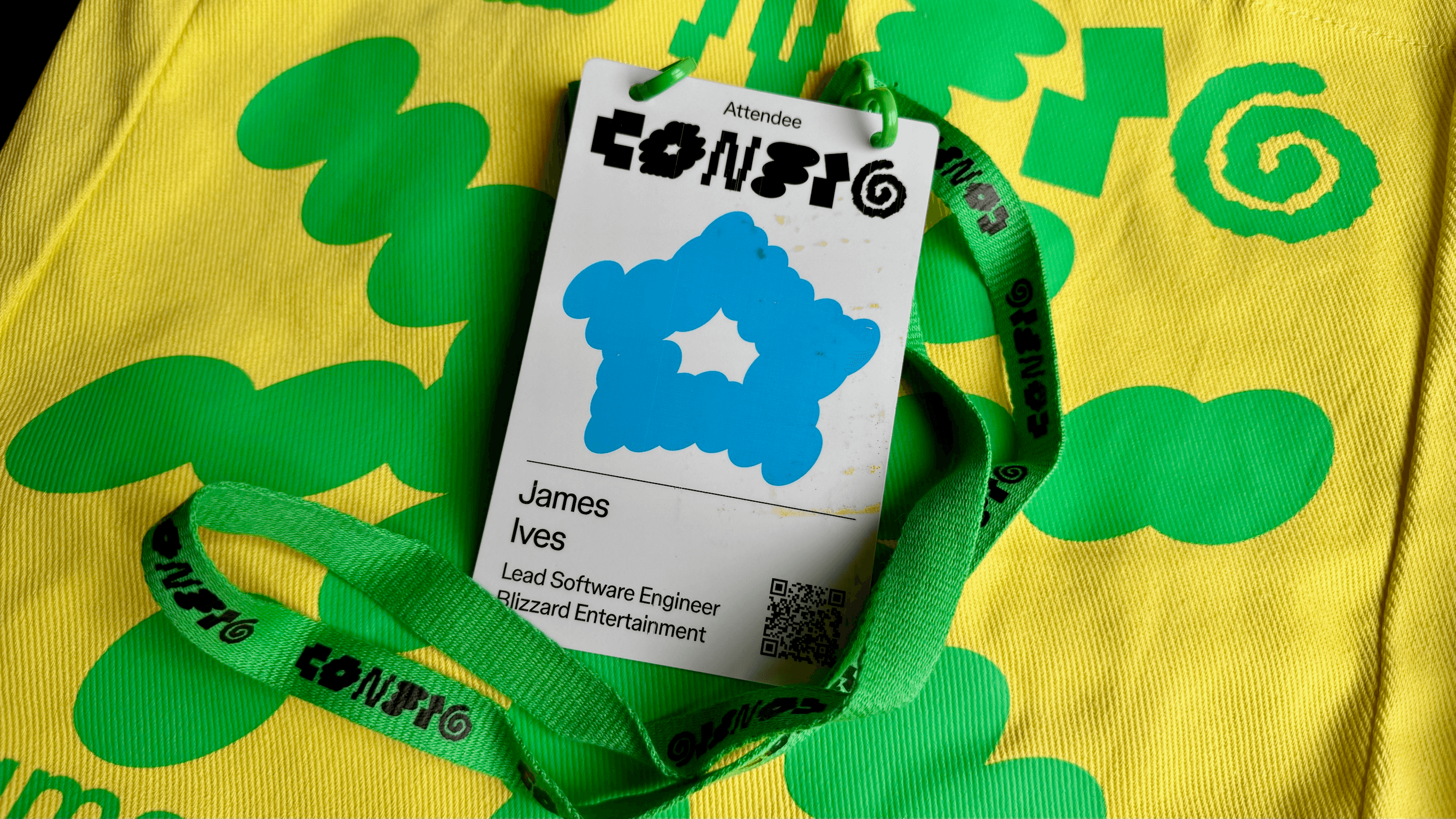 A Config 2026 attendee badge for James Ives, Lead Software Engineer at Blizzard Entertainment, on a green lanyard resting on a yellow tote bag