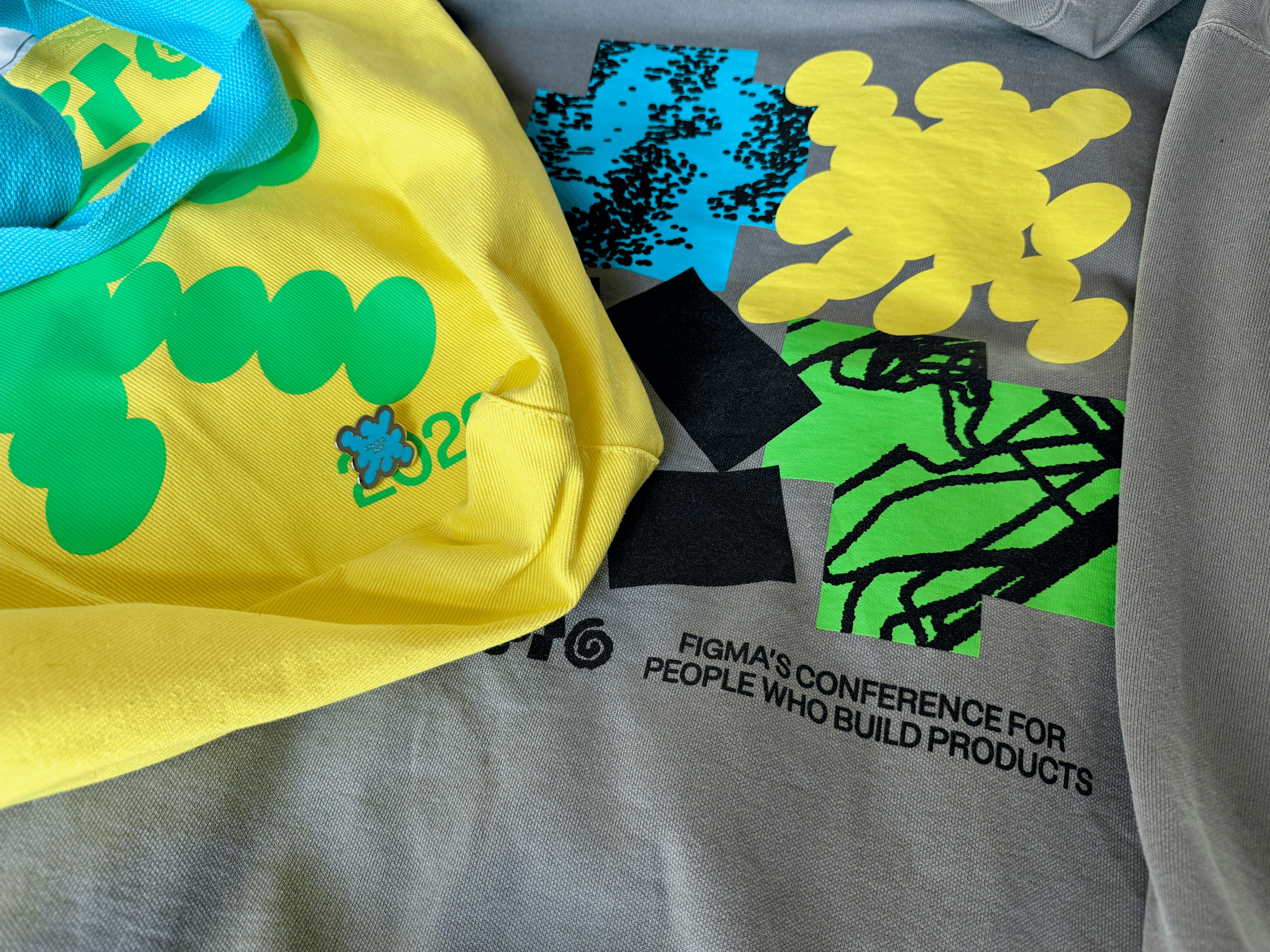 A grey Config 2026 jumper reading 'Figma's conference for people who build products' next to a yellow Config tote bag