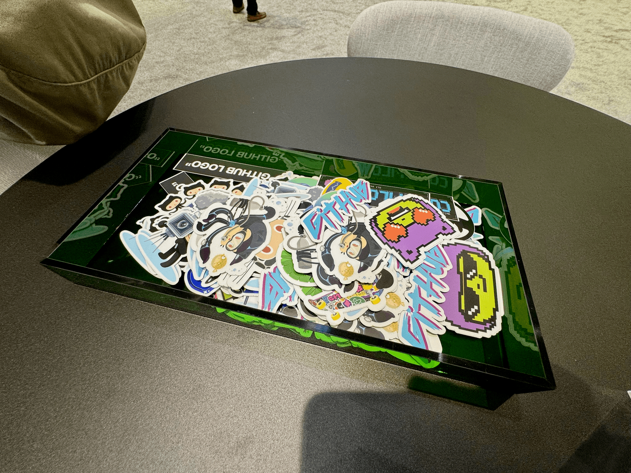 A pile of colourful GitHub-branded stickers in a tray on a table at the GitHub booth
